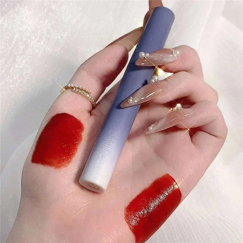 Close-up of hand with two swatches of vibrant red matte lipstick and holding a sleek lavender lipstick tube from the Matte Lipstick Set
