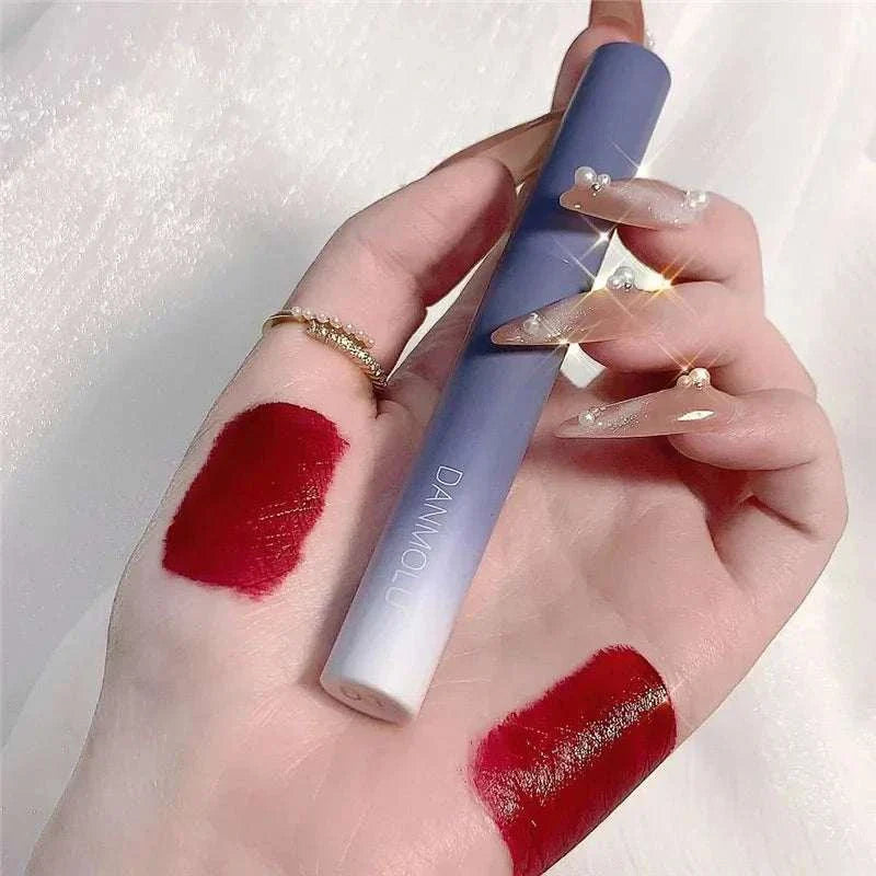 Matte Lipstick Set showing rich red shade swatches on hand with sleek blue-gray lipstick tube held between fingers with pearl-accented nails