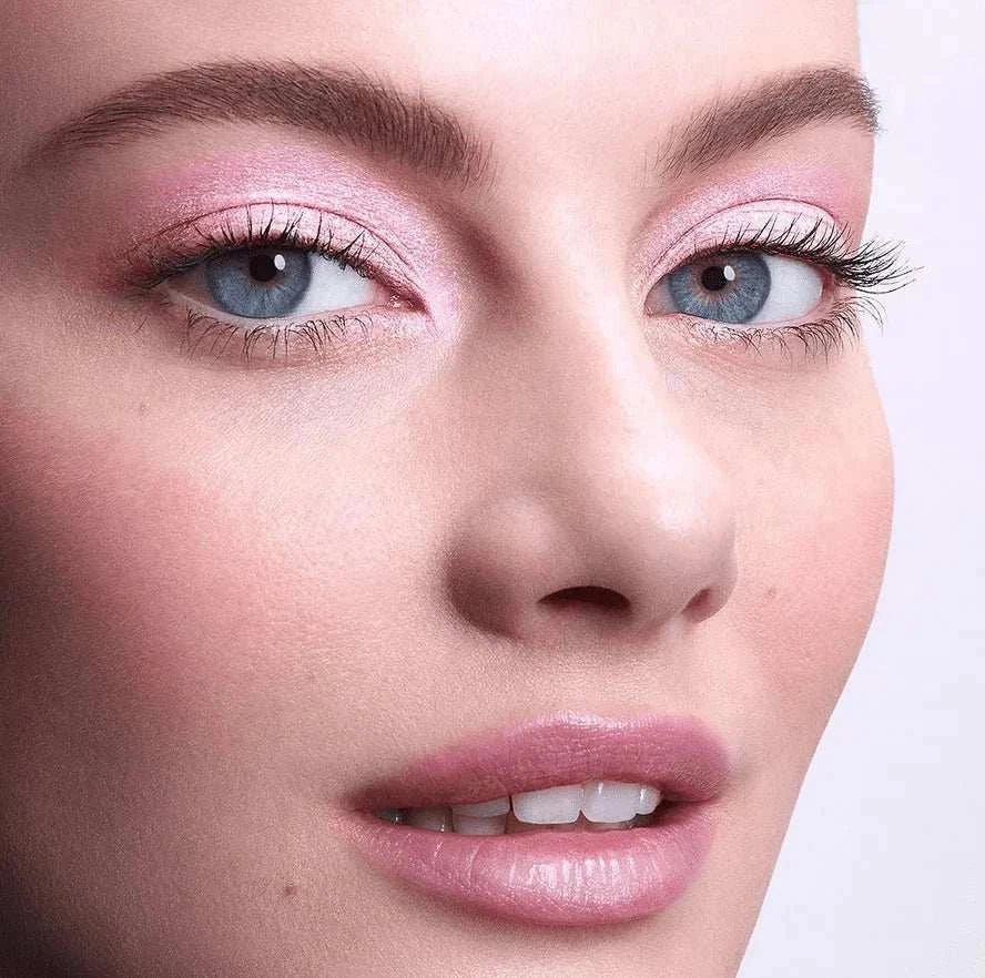 Close-up of a woman's face with pink shimmering highlighter on eyelids and cheeks, showcasing a radiant and glowing makeup look.