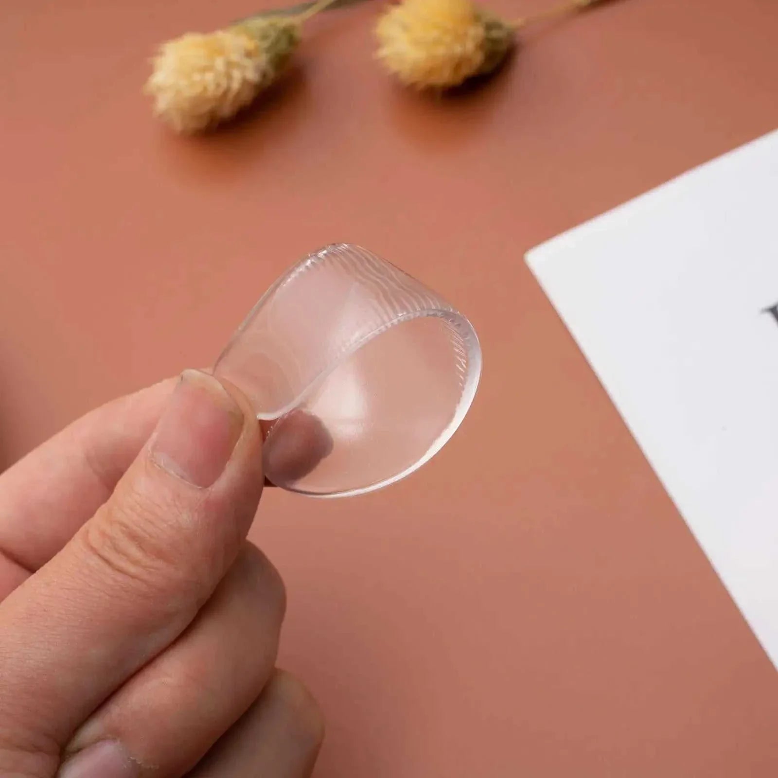 Reusable Anti-Wrinkle Forehead Patch made of soft, medical-grade silicone held between fingers against a brown background
