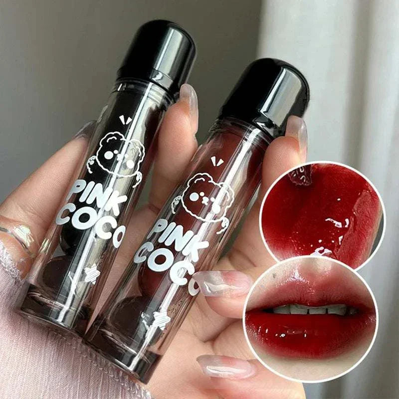 Two PINKCOCO Bear Doodle Mirror Lip Glaze tubes held in hand with close-up of glossy red lip application and texture.