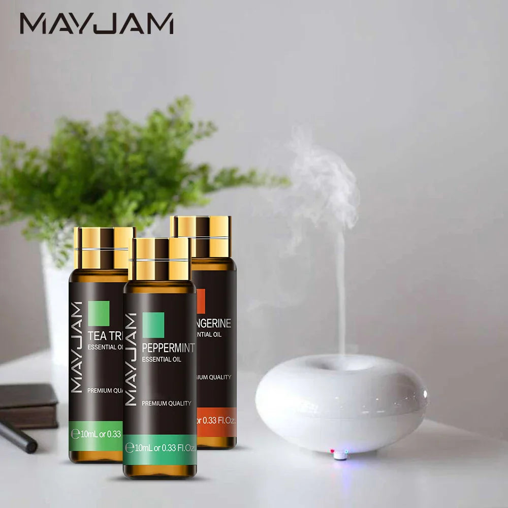 MAYJAM Essential Oil bottles with dropper, including Tea Tree, Peppermint, and Tangerine scents, beside a white diffuser releasing mist in a calming home setting