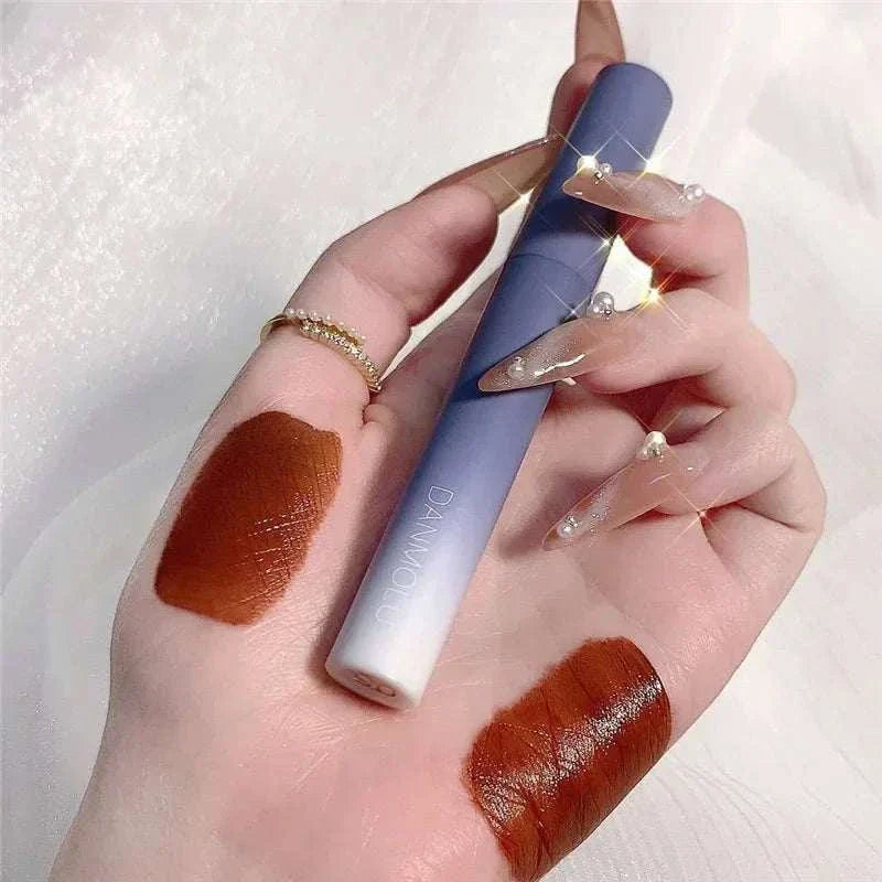 Hand holding a matte lipstick with two swatches of deep brown color on skin, showcasing the Matte Lipstick Set's rich pigment and smooth finish.