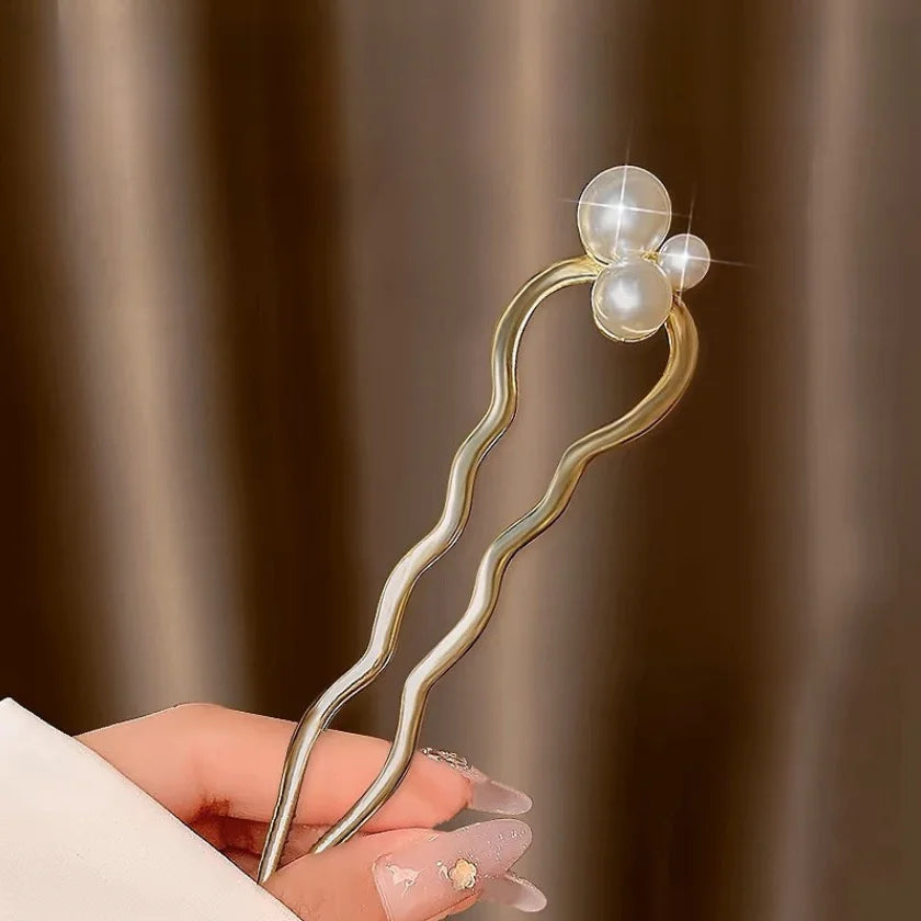 Pearl U-shaped hairpin with metallic shell and delicate pearl accents held in hand against a brown background