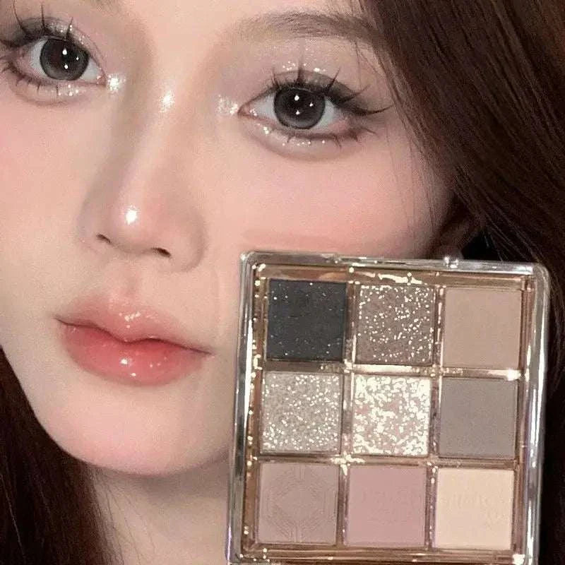 Close-up of a woman holding a 9 Colors Eyeshadow Palette featuring matte and shimmery neutral shades including black, grey, and beige.