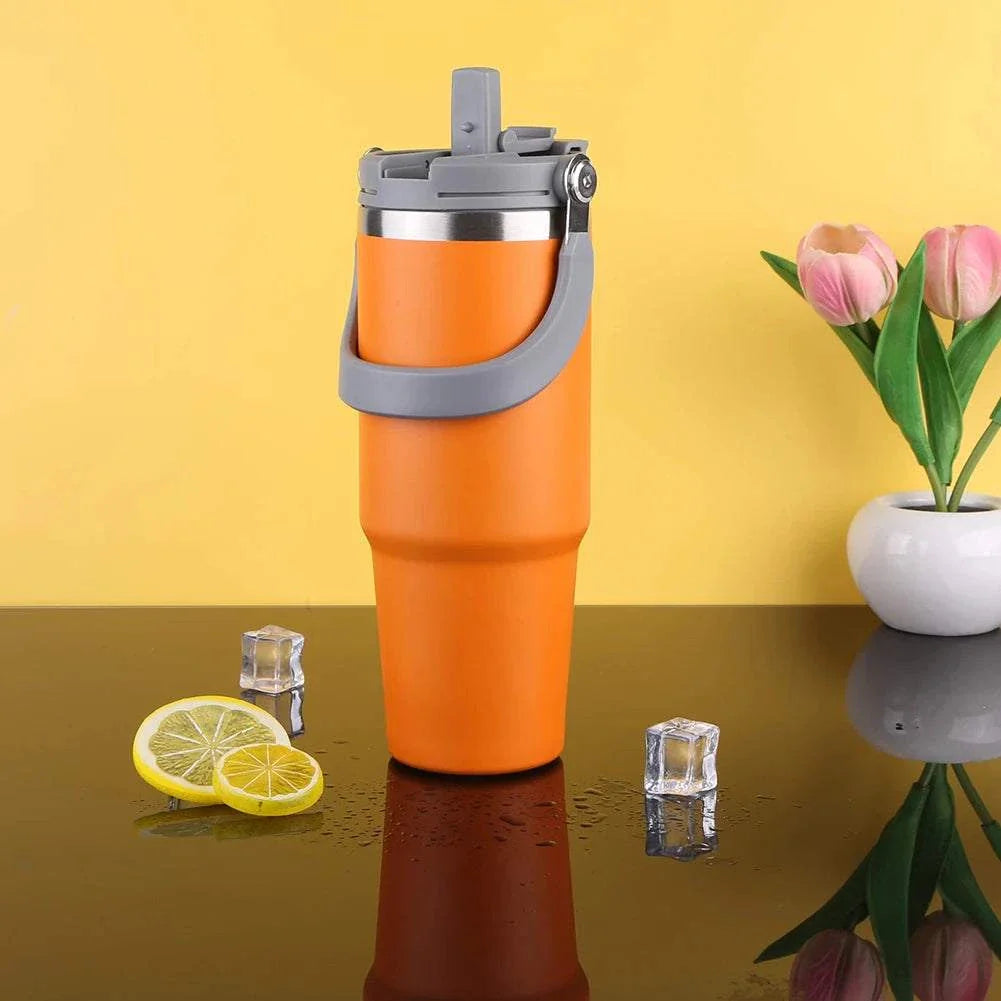 Orange 30oz vacuum insulated cup with handle on black surface with lemon slices and ice cubes, next to vase with pink tulips