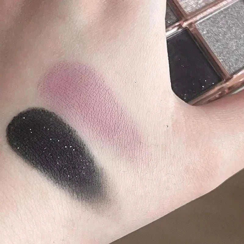 Swatches of black and mauve shades from 9 colors eyeshadow palette on skin with palette visible in background