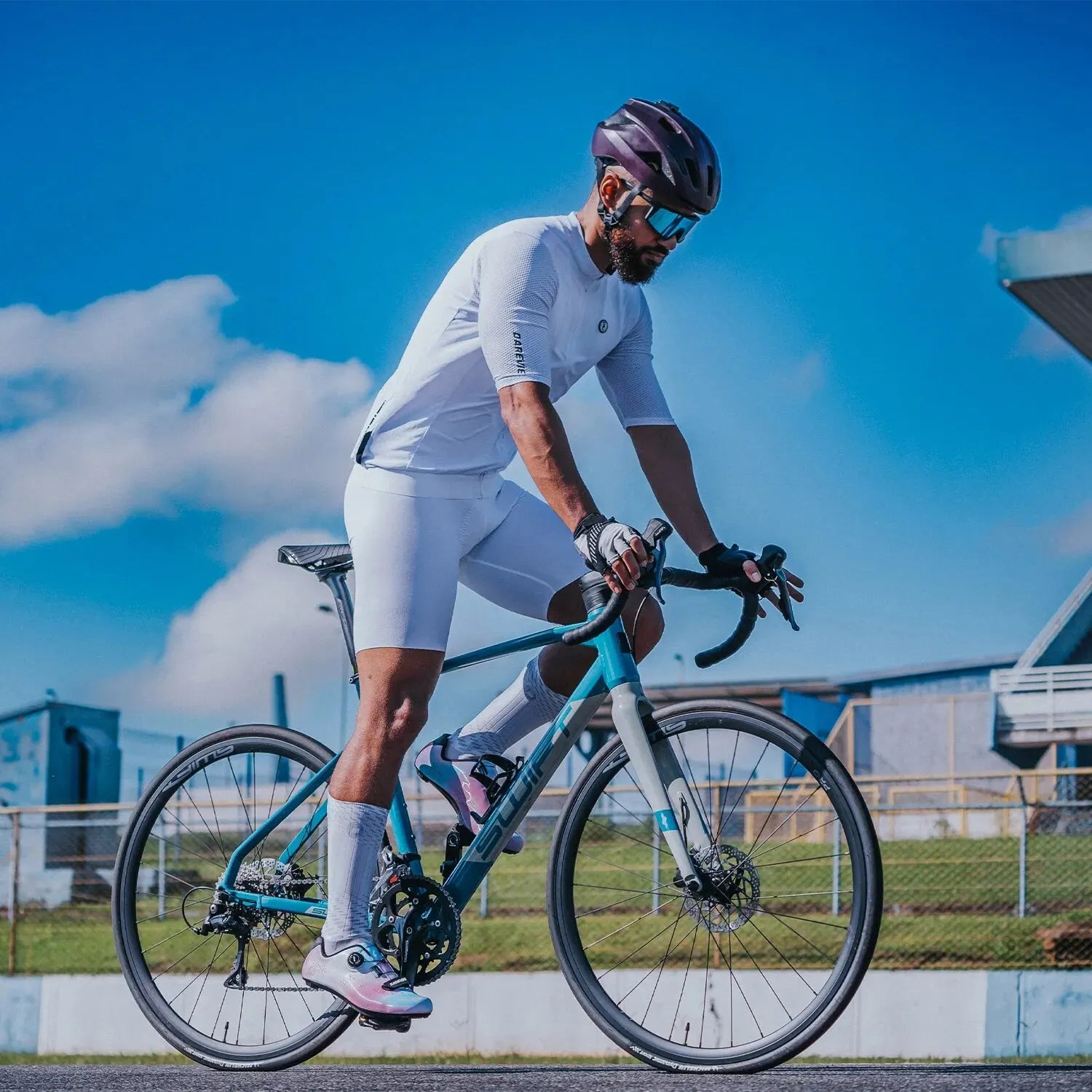 Man cycling outdoors wearing DAREVIE Cycling Jersey and shorts on a road bike under blue sky