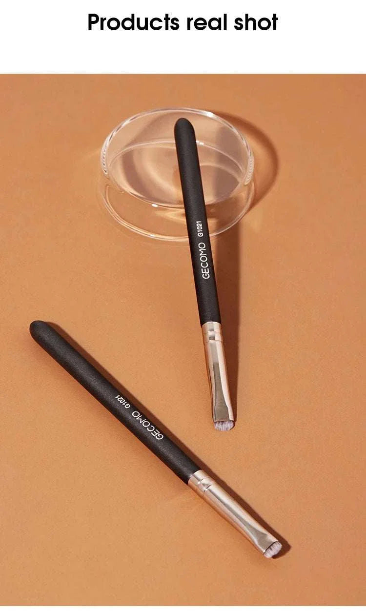 Eyeliner and eyebrow makeup brush set with black handles and silver ferrules on a brown surface