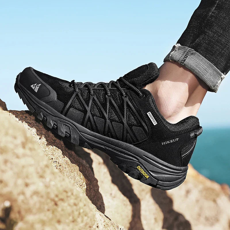 Black HIKEUP men's hiking shoe with durable construction, superior grip sole, breathable mesh, and comfortable cushioning, worn on rocky terrain outdoors.