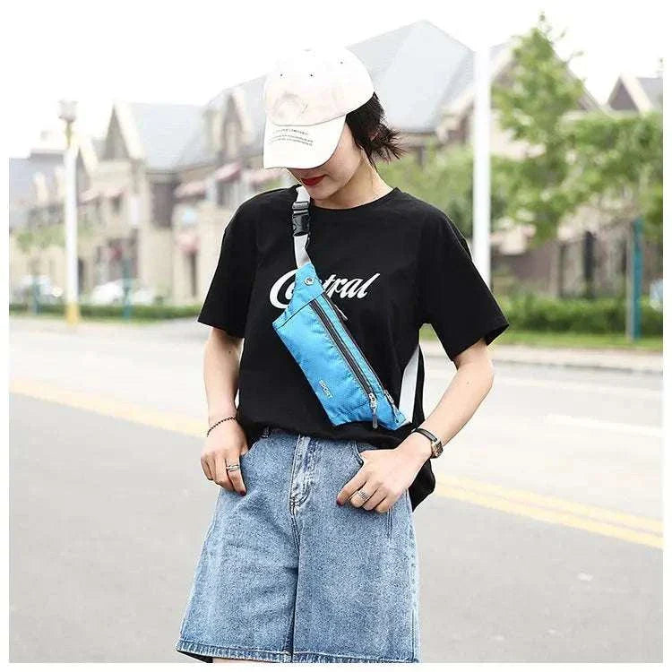 Person wearing a blue nylon waist and chest bag across the chest with casual black t-shirt and denim shorts outdoors