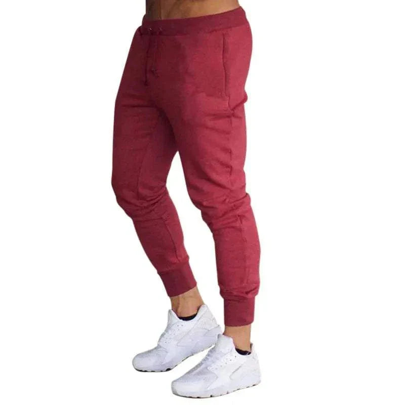 Men's Training Jogger Sweatpants in red with tapered fit and elastic waistband, styled with white sneakers.