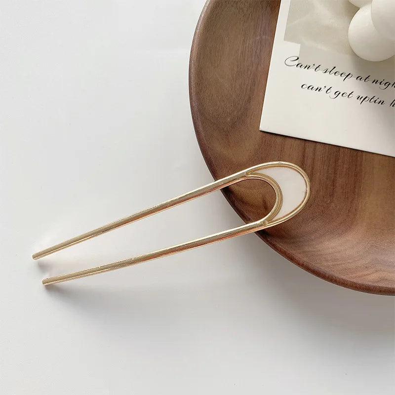 Pearl U-shaped hairpin with metallic shell detail on wooden plate for elegant hairstyles