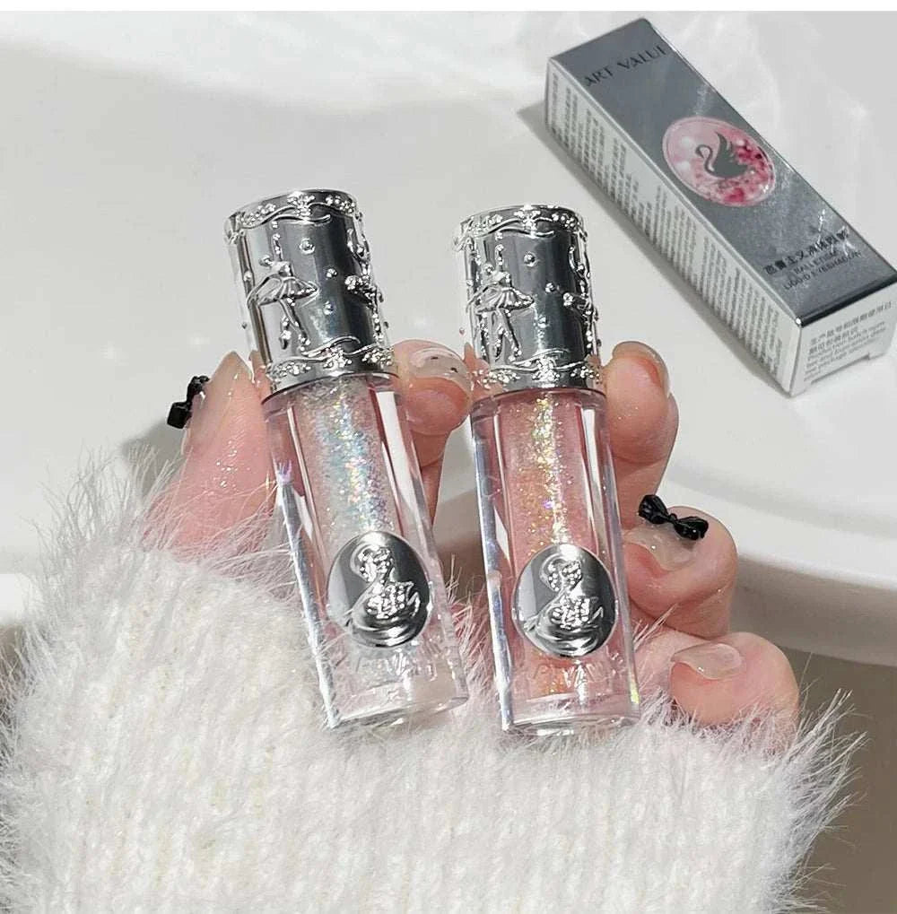 Two elegant Balletism liquid eyeshadow bottles with fine shimmer highlight held in a hand, featuring silver caps and transparent packaging showing iridescent pink and white shades, with product box in the background.