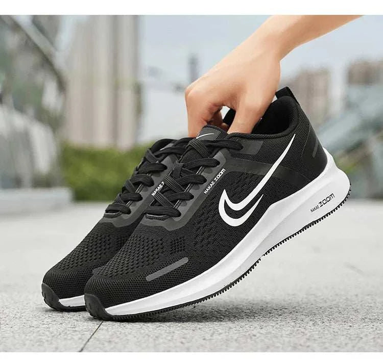 Black men's lightweight running shoes with breathable mesh and non-slip white soles being held by a hand outdoors