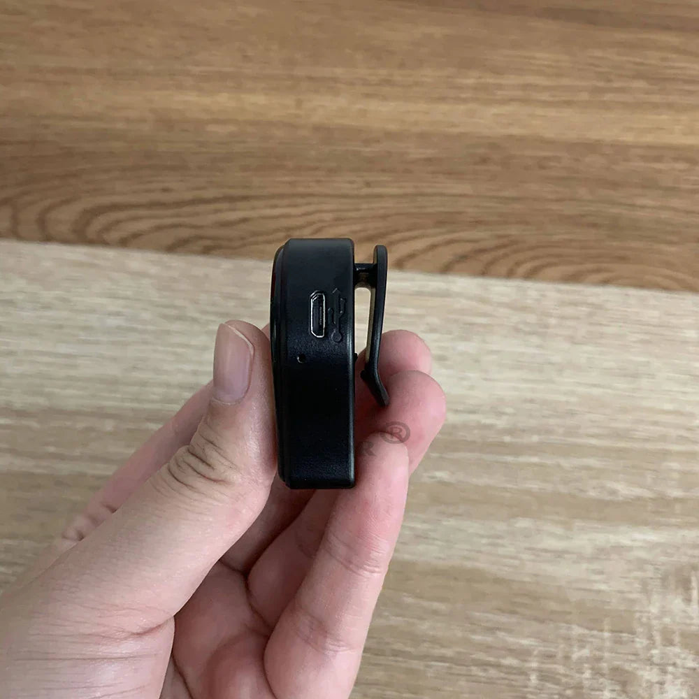 Close-up of black Auto Catch Powermon Go Plus Bluetooth wristband with USB charging port held in hand against wooden background