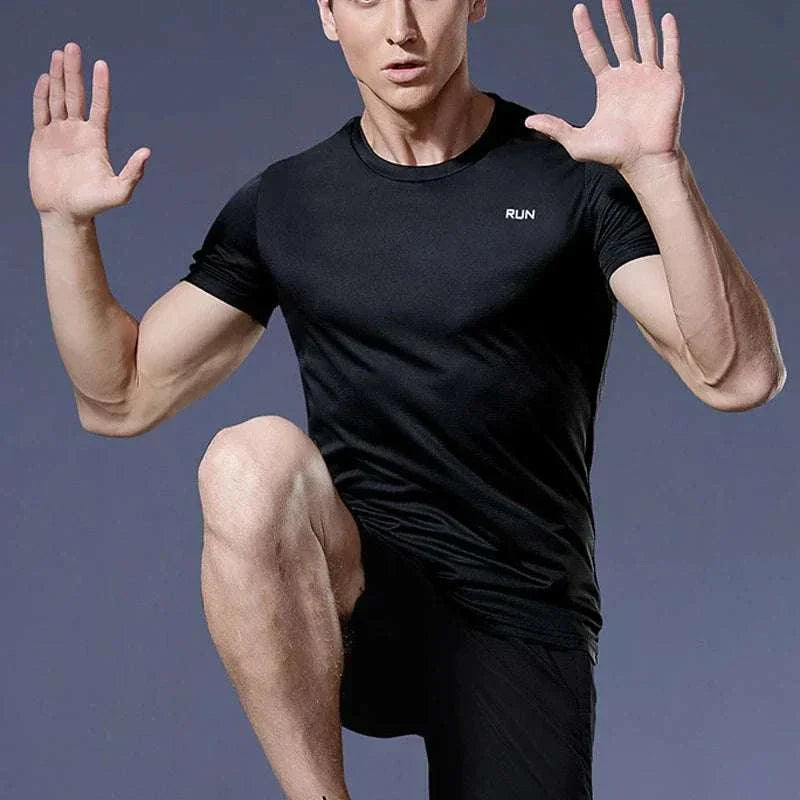 Man wearing black men's quick-dry compression sport t-shirt in athletic pose against gray background
