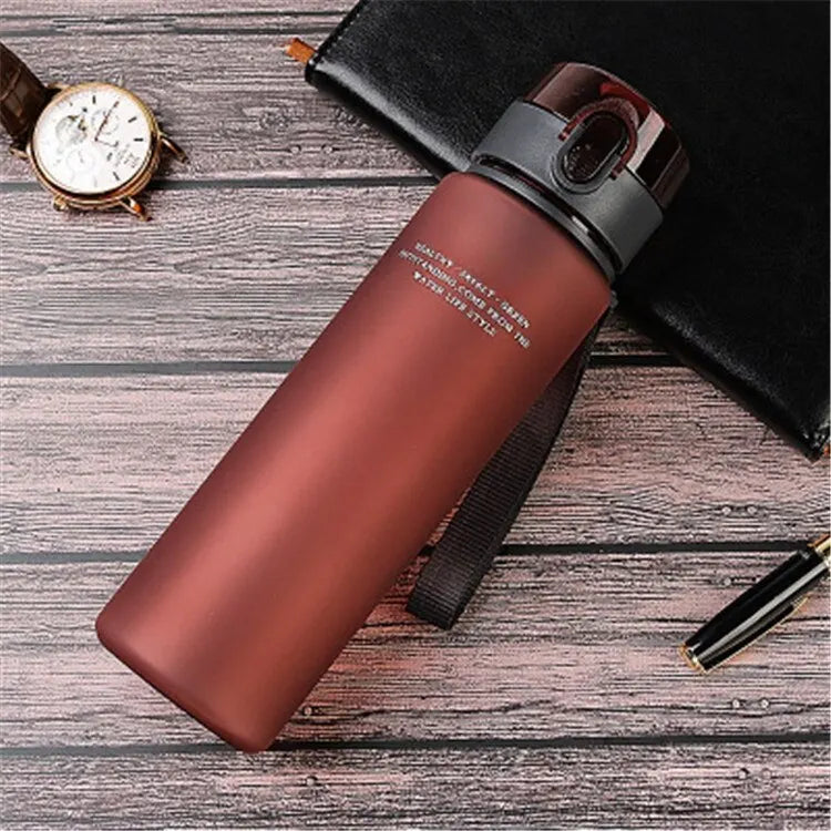 BPA-Free leak-proof sports water bottle in matte brown with secure screw-top lid and wrist strap on wooden surface.