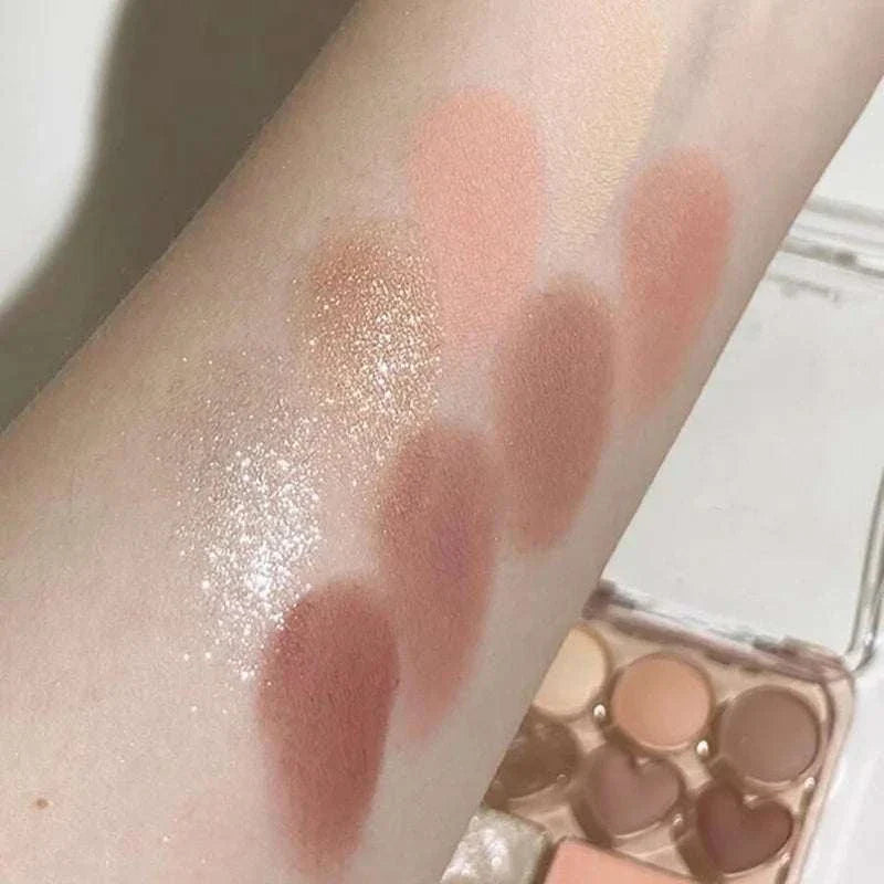 Swatches of 8-Color Pink Orange Eyeshadow Palette showcasing pink, orange, peach, and shimmery shades on arm with heart-shaped compact visible.