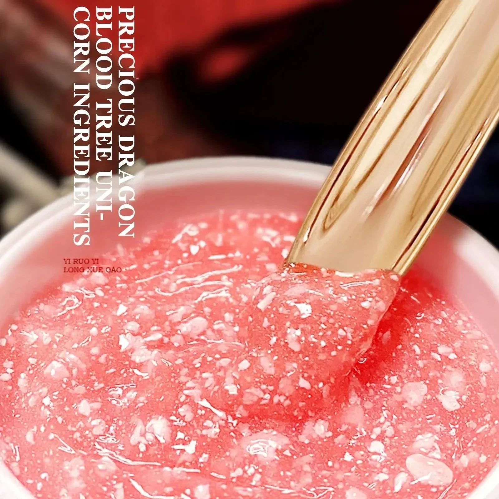 Close-up of pink Dragon’s Blood Face Cream with a gold spatula showing its textured gel formula with white particles.