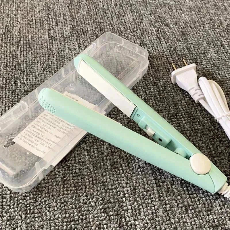 Compact mint green mini flat iron for travel with white power cord and clear plastic case on gray carpet