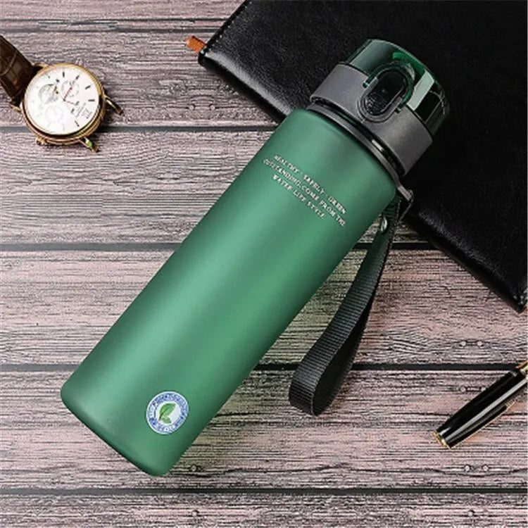 Green BPA-free leak-proof sports water bottle with black strap on wooden surface next to watch, pen, and black wallet