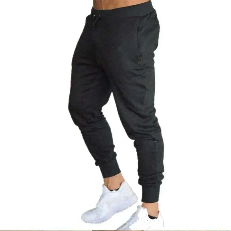 Black men's training jogger sweatpants with tapered fit, elastic waistband, and drawstring, paired with white sneakers.