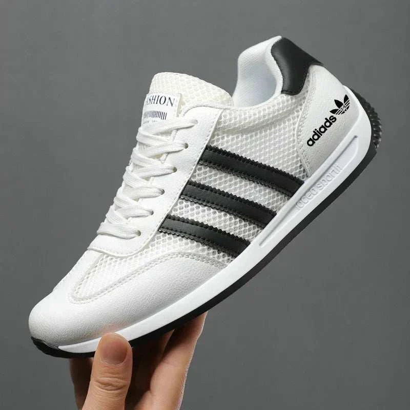 White and black men's casual sport shoe with breathable mesh upper and flexible sole held in hand against gray background