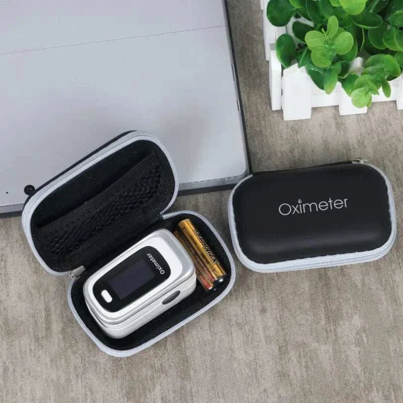 Black zippered carrying case for oximeter device with batteries and mesh pocket inside, placed on wooden surface next to green potted plant