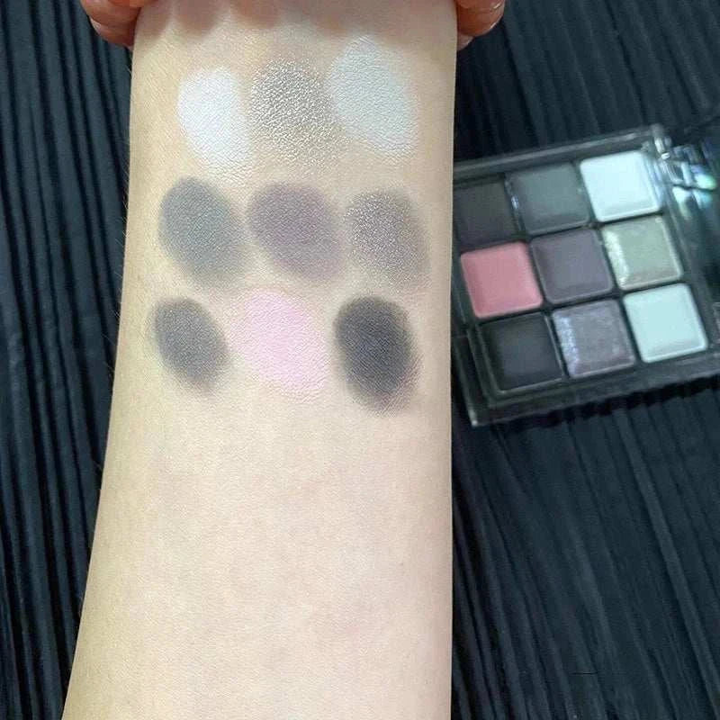 Black Pink Smoky Eye Shadow Palette swatches on arm showing matte and pearlescent shades in black, pink, and chocolate tones with palette in background