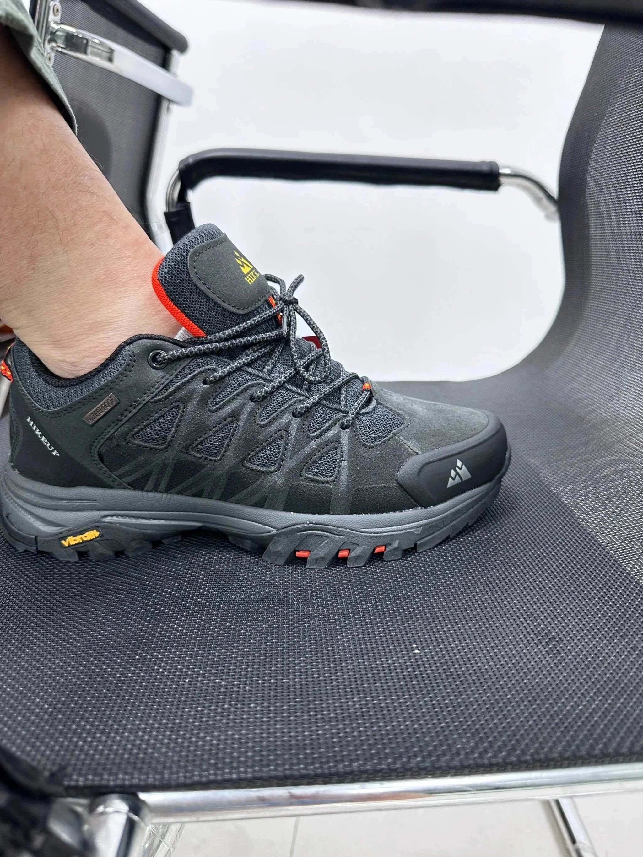 Men's Hiking Shoes in black with red accents, designed for durability and comfort, shown worn on a foot resting on an office chair seat.