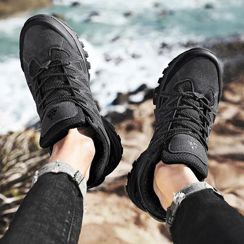 Men's black hiking shoes with durable construction and high-traction soles, worn outdoors on rocky terrain