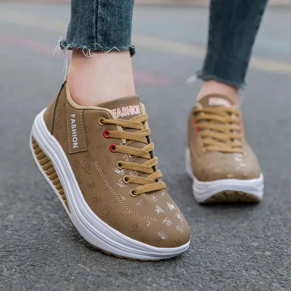 Brown breathable wedge heel sneakers with thick cushioned sole and lace-up closure worn with jeans on pavement