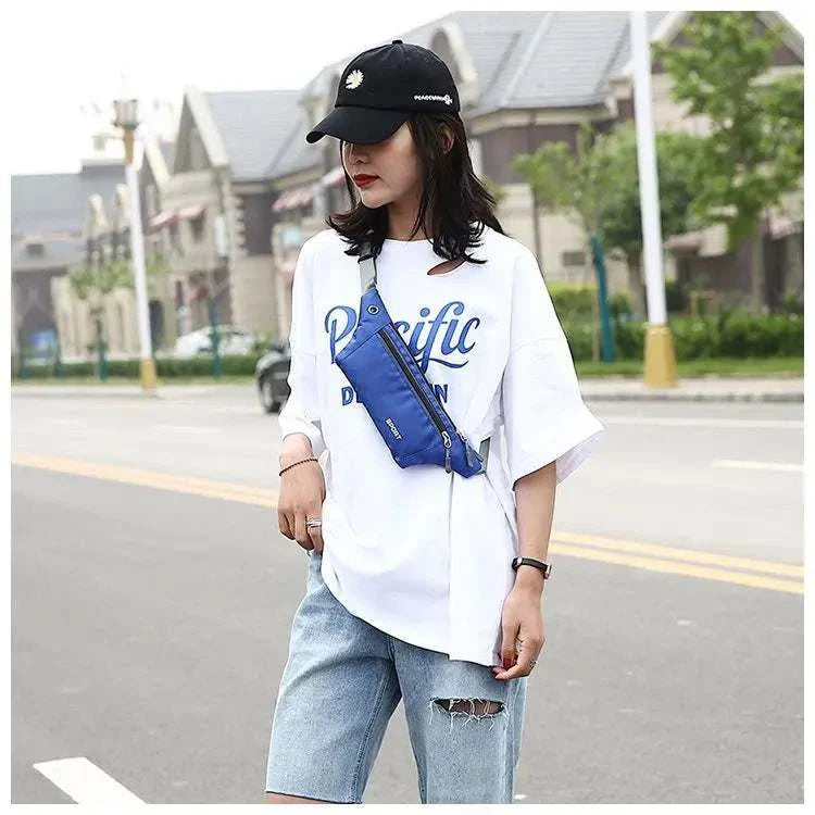 Woman wearing blue nylon waist and chest bag crossbody style with casual white t-shirt and denim shorts outdoors