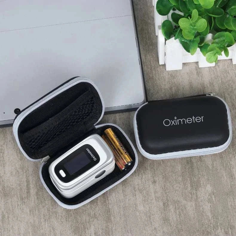 Compact black carrying case with portable oximeter device and batteries inside on wooden surface near green plant