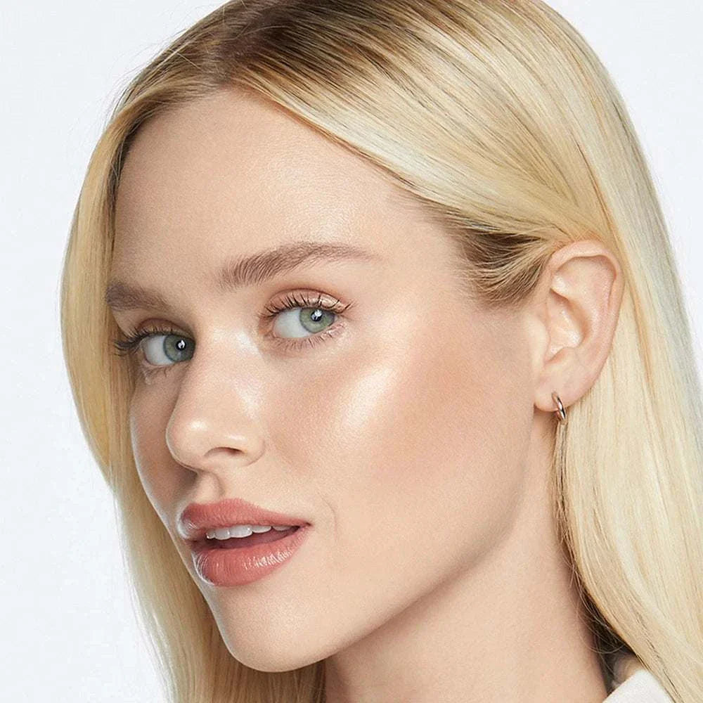 Close-up of a woman with blonde hair showcasing radiant and glowing skin using Face & Body Shimmering Highlighter makeup.
