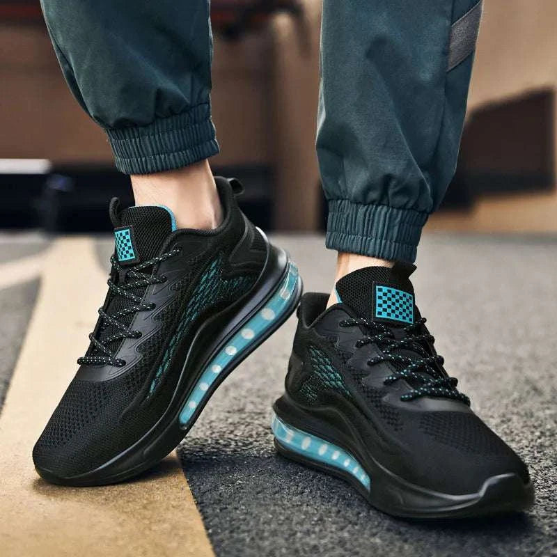 Breathable unisex sneaker with black mesh upper, cushioned sole, and blue air sole units, worn with dark jogger pants on street surface