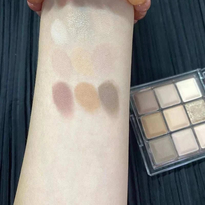 Swatches of Black Pink Smoky Eye Shadow Palette featuring matte and pearlescent neutral and warm brown shades on arm next to compact case
