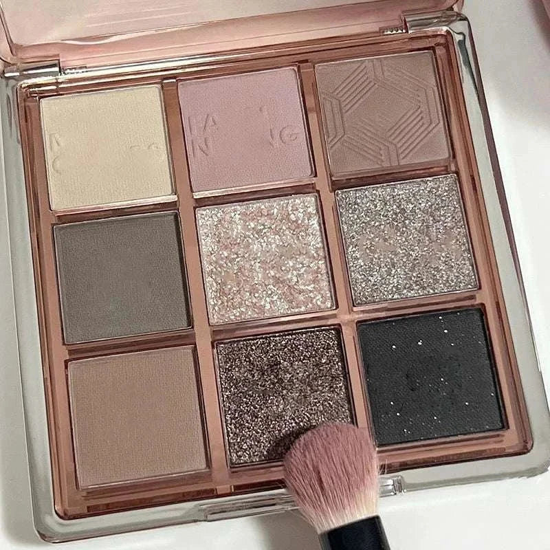 9 Colors Eyeshadow Palette featuring matte and glitter shades in neutral, pink, gray, and black tones with a makeup brush.