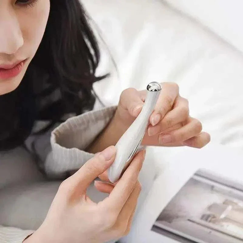Woman using home electric eye massage beauty instrument for reducing puffiness and fine lines.
