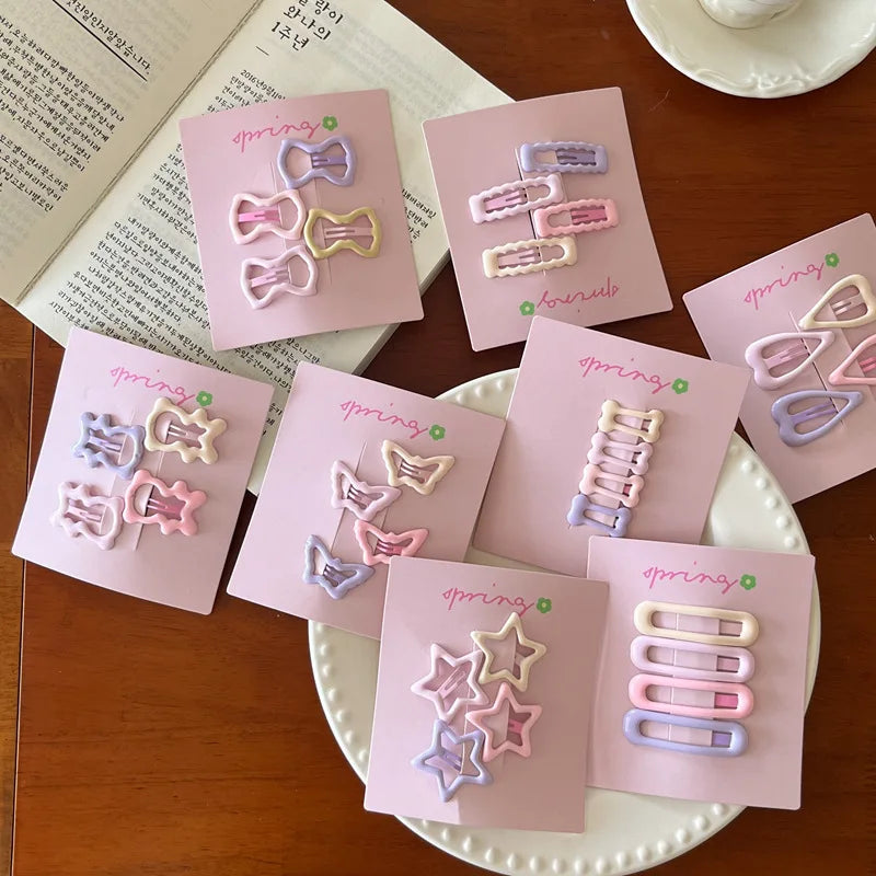 Set of 4 cute colorful geometric mini hair clips for kids on pink cards displayed on a wooden table and white plate