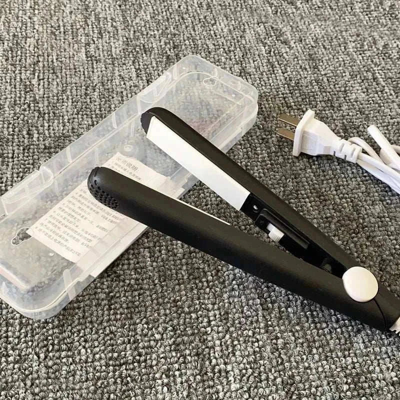 Compact black mini flat iron with white ceramic plates, clear plastic travel case, and white power cord on gray carpet, ideal for travel styling.